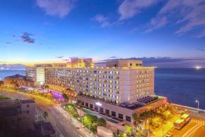 a large white building next to the ocean at night at Ramada Plaza by Wyndham Jeju Ocean Front in Jeju