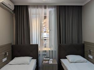 2 łóżka w pokoju hotelowym z oknem w obiekcie Victoria Hotel w mieście Uralsk