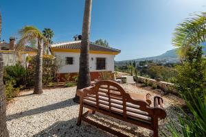 a bench in front of a house with palm trees at Casa Amarilla Casitas in Alhaurín el Grande