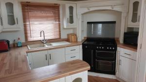 La cuisine est équipée de placards blancs et d'un four avec plaques de cuisson noires. dans l'établissement 2 bedroom caravan near Llanberis, on the edge of Snowdonia, à Llanddeiniolen