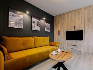 a living room with a yellow couch and a table at VacationClub - Apartamenty Zakopiańskie Apartament 437 in Zakopane