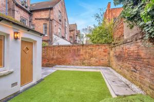 a courtyard with green grass next to a brick wall at Comfortable flat by MT Property in Nottingham