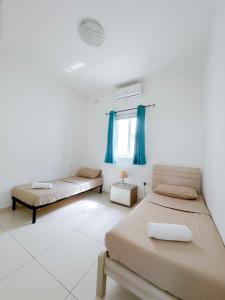 Duas camas num quarto branco com cortinas azuis em Lovely flat close to St julians with 6 beds in 3 rooms for 8 people em Is-Swieqi