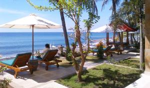 un hombre sentado en una silla bajo una sombrilla en la playa en Apa Kabar Villas, en Amed