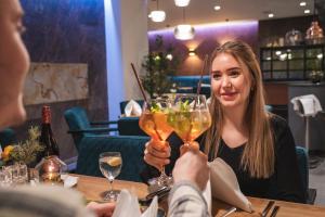 a woman sitting at a table with two people holding wine glasses at Parkhotel Flora in Bad Grund