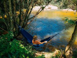 a boy laying in a hammock on a river at Suíte de Vidro com Cachoeira no Quintal in Antônio Carlos
