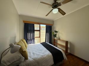 a bedroom with a bed with a ceiling fan and a window at Loddeys Beach House - by Beach Collection in Strand