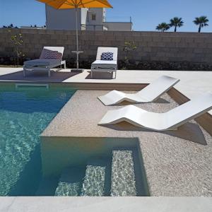 - une piscine avec 2 chaises blanches et un parasol dans l'établissement CasaKarina - Villa con piscina privata, à Specchia