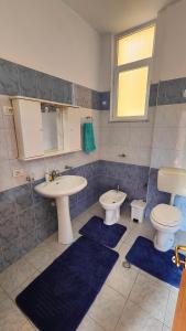 a bathroom with two sinks and a toilet and blue rugs at Appartamento Bruno spazioso e centrale in Shkodër +6 photos