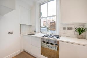 cocina blanca con fogones y ventana en Charming 1 Bedroom Flat with Private Patio - West London, Kensington, Earl's Court, Chelsea en Londres