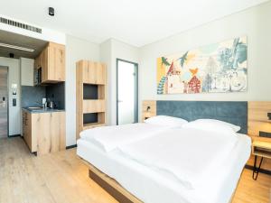 a bedroom with a white bed and a kitchen at B&B HOTEL Albstadt-Hbf in Albstadt