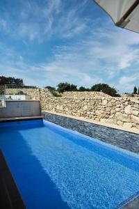 a blue swimming pool next to a stone wall at Charming and Tranquil House in Għasri