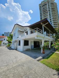a white house with a balcony and a tall building at Little Heaven by Sky Hive, A Beach Front Bungalow in Tanjung Bungah