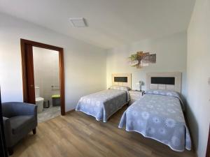 1 dormitorio con 2 camas, silla y espejo en Habitaciones A Casa de Pepe, en Triacastela