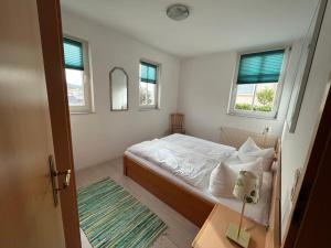 a small bedroom with a bed and two windows at Apartmenthaus Aurum in Ahlbeck
