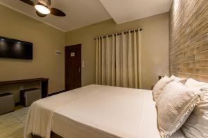 Schlafzimmer mit einem weißen Bett und einem Flachbild-TV in der Unterkunft Villa Ayê Socorro SP - Pousada Petfriendly in Socorro