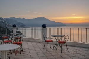 un gruppo di tavoli e sedie su un balcone con vista sull'oceano di Hotel Le Terrazze a Conca dei Marini