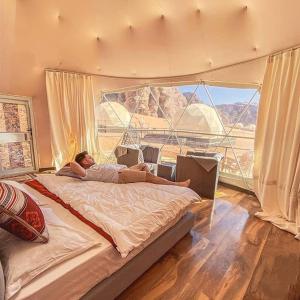 desert wadi rum camp في وادي رم: رجل يستلقي على سرير في غرفة ذات نافذة كبيرة