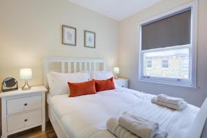 a bedroom with a white bed with orange pillows and a window at Stunning 4 Bedroom House in London