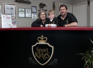 Um homem, uma mulher e uma criança atrás de um balcão. em Sport Of Kings Motel em Rotorua