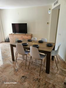 a dining room table with white chairs and a television at Piso acogedor en Alcaucin in Alcaucín