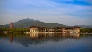 a building on a lake with mountains in the background at Yanqi Hotel, Managed by Kempinski in Huairou