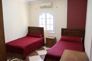 2 Betten in einem Zimmer mit roter Bettwäsche und einem Fenster in der Unterkunft Sandy House in Madinat as-Sadis min Uktubar
