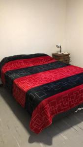 a red and black bed with a lamp on a table at Cómodo Departamento Hogareño in San Carlos de Bariloche