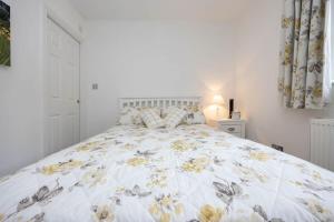 Dormitorio blanco con cama con colcha de flores en Countryside Cottage with Stunning Views en Fletching