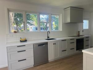 a white kitchen with white cabinets and windows at Village Cottage in Havelock North