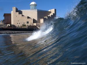 a wave in the ocean with a lighthouse in the background at Bluebeach in Las Palmas de Gran Canaria