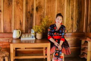 una mujer sentada en una mesa de madera en una habitación en Hoa Lan Bungalow & Restaurant, en Phong Thổ