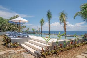 a swimming pool with chairs and an umbrella and the ocean at Ocean Paradise Bali in Buleleng