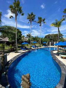 a large swimming pool with blue water and palm trees at Balangan Surf Resort in Jimbaran