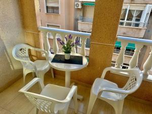 a balcony with white chairs and a table with flowers at La Loma 72 in Torrevieja