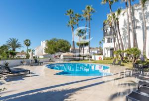 a swimming pool with palm trees and a building at Jardines de las Golondrinas in Marbella