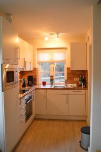 eine Küche mit weißen Schränken, einem Waschbecken und einem Fenster in der Unterkunft Green Eilun - Hausteil 5 in Wyk auf Föhr