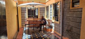 Ein Mann, der an einem Tisch unter einem Schirm sitzt. in der Unterkunft Zedek Furnished Apartment 102 in Nairobi
