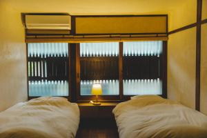 ein Schlafzimmer mit 2 Betten und ein Fenster mit einer Lampe in der Unterkunft Masukichi 古民家宿ますきち 駐車場無料 in Seto