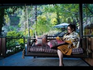 SaffronStays Ekam Walnut Suite, Chail في Kandāghāt: امرأة جالسة على أرجوحة تقرأ كتابا