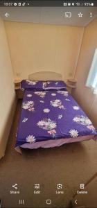 Una cama con un edredón púrpura con flores. en Elle en Mablethorpe