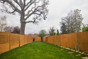 a fence in a yard with a tree behind it at The Enfield Place - Elegant 4BDR House with Garden in Winchmore Hill