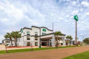 een groot wit gebouw met palmbomen voor een weg bij Wingate by Wyndham Sulphur Near Lake Charles in Sulphur