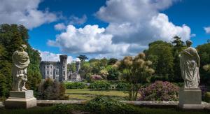 zwei Statuen in einem Garten mit einem Schloss im Hintergrund in der Unterkunft Clearwater Cove Rosslare Stand County Wexford in Walsheslough