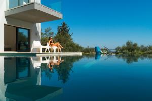 una mujer sentada en una silla junto a una piscina en The Designer's Villa - Member of Spiritual Living Corfu en Virós