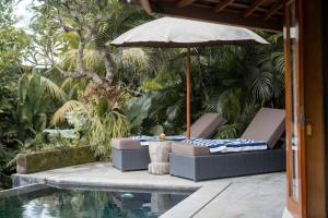 a patio with a table and an umbrella next to a pool at The Sender Pool Suites in Ubud