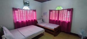a small room with two beds and pink curtains at Camille's Cheapstay in Alaminos