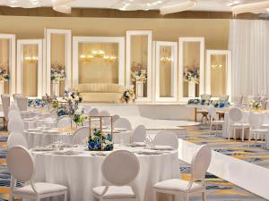 a banquet hall with white tables and white chairs at Mövenpick Hotel & Apartments Ghala Muscat in Muscat