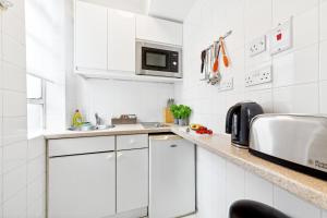 cocina blanca con fregadero y microondas en Nell Gwynn Chelsea Accommodation, en Londres