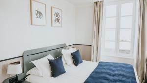 a bedroom with a bed with blue and white pillows at Hôtel De La Marine in Arromanches-les-Bains